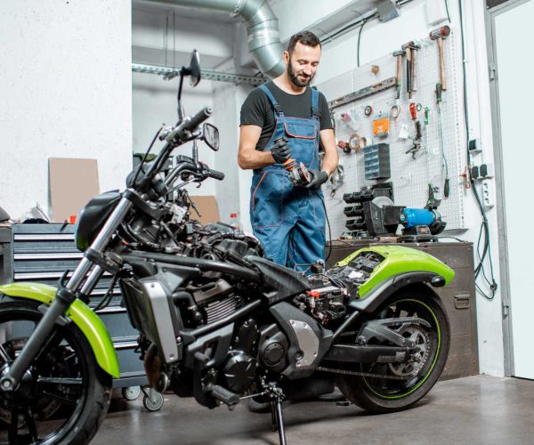 Portrait of a biker or repairman in working overalls standing near the motorcycle during the repairment in the workshop